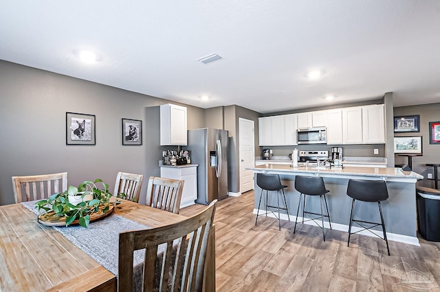 kitchen with a breakfast bar, a kitchen island with sink, appliances with stainless steel finishes, light hardwood / wood-style floors, and white cabinetry