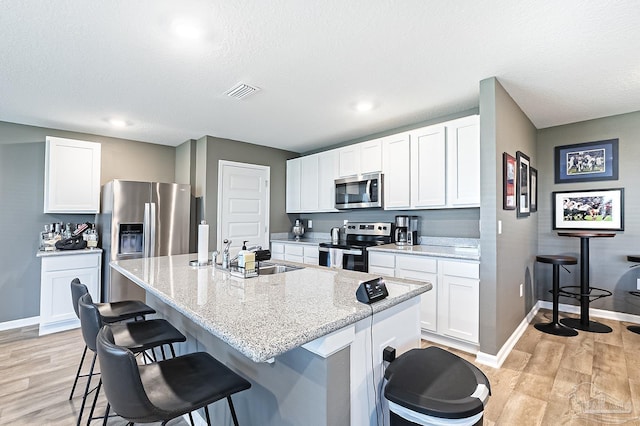 kitchen featuring sink, an island with sink, appliances with stainless steel finishes, light hardwood / wood-style floors, and white cabinetry