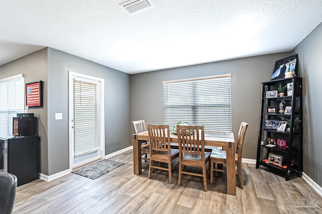 dining room with plenty of natural light, a textured ceiling, and light hardwood / wood-style flooring