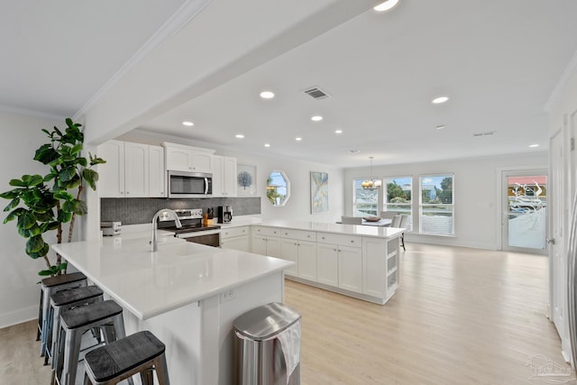 kitchen with backsplash, white cabinets, appliances with stainless steel finishes, decorative light fixtures, and a breakfast bar area