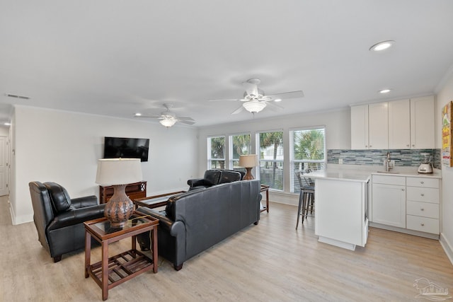 living room with light hardwood / wood-style flooring, ceiling fan, crown molding, and sink