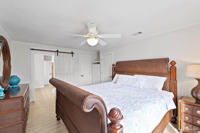 bedroom featuring a barn door, light hardwood / wood-style floors, ceiling fan, and ornamental molding