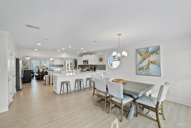 dining space featuring light hardwood / wood-style flooring, ceiling fan with notable chandelier, and ornamental molding