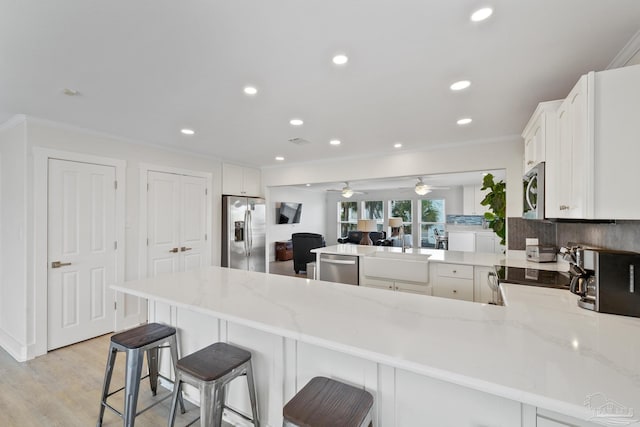 kitchen with light stone countertops, kitchen peninsula, a breakfast bar area, white cabinets, and appliances with stainless steel finishes