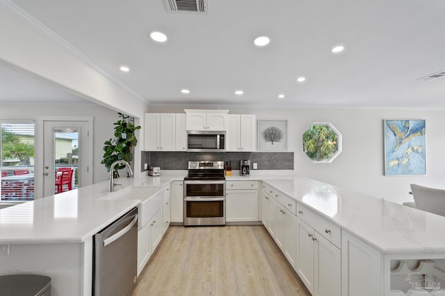 kitchen with backsplash, kitchen peninsula, sink, appliances with stainless steel finishes, and white cabinetry