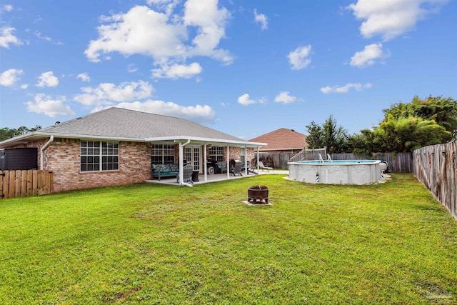 rear view of house featuring a fenced in pool, a lawn, a patio, and an outdoor fire pit