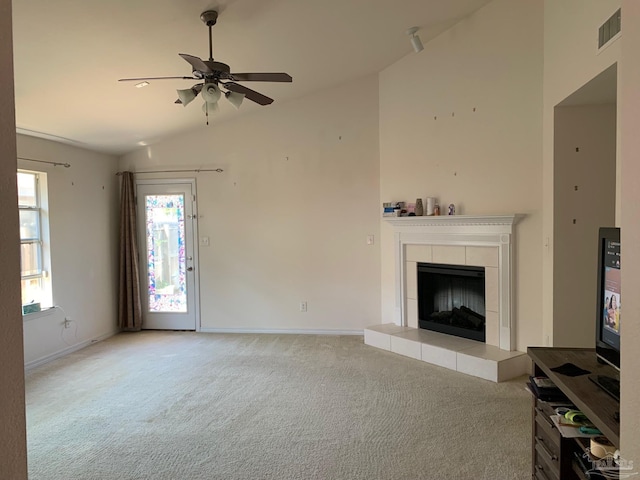 unfurnished living room with ceiling fan, vaulted ceiling, a tile fireplace, and light colored carpet