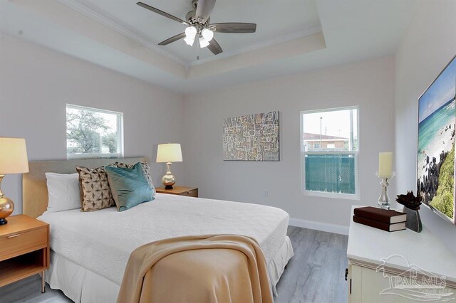 bedroom featuring hardwood / wood-style flooring, ceiling fan, ornamental molding, and a tray ceiling