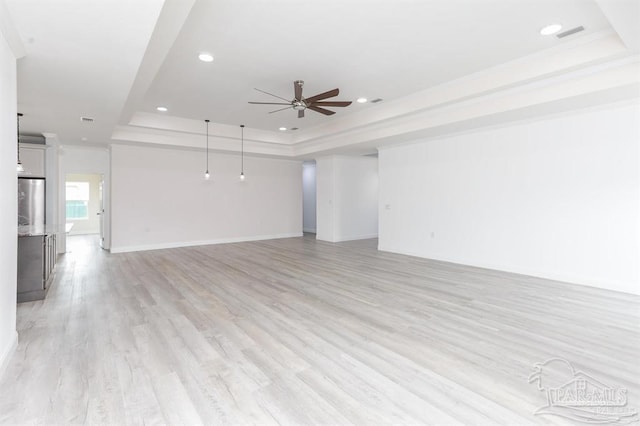 unfurnished living room with a tray ceiling, ceiling fan, crown molding, and light wood-type flooring