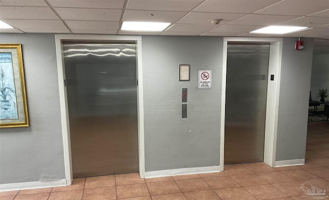 corridor featuring light tile patterned floors, a paneled ceiling, and elevator