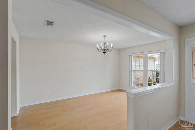 empty room featuring a textured ceiling, baseboards, visible vents, light wood-style flooring, and a notable chandelier
