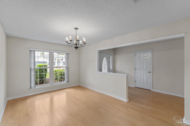 spare room featuring light wood finished floors, a textured ceiling, baseboards, and a notable chandelier