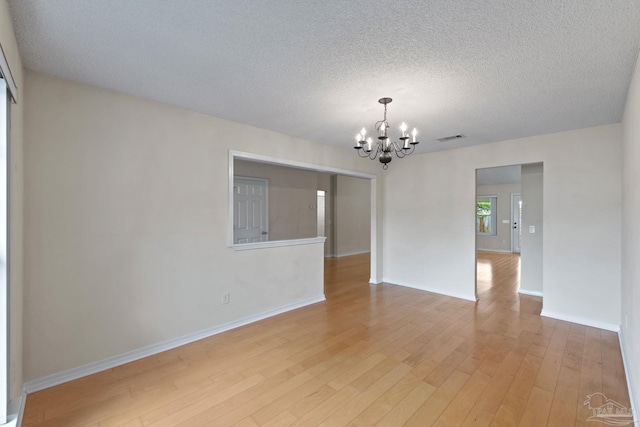 spare room featuring a textured ceiling, visible vents, a chandelier, light wood-style flooring, and baseboards