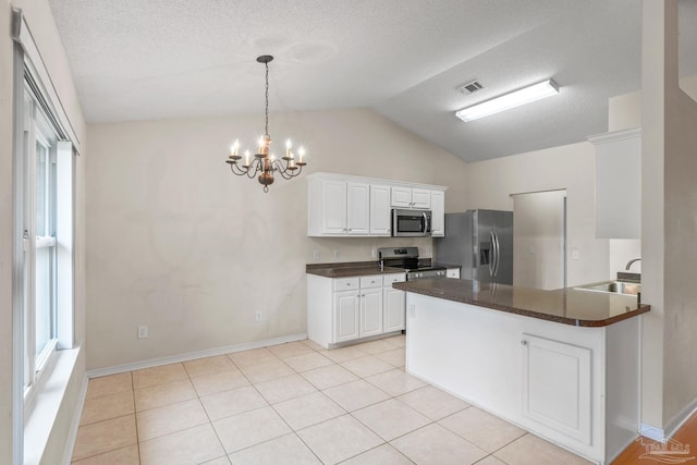 kitchen with a sink, dark countertops, a notable chandelier, appliances with stainless steel finishes, and lofted ceiling