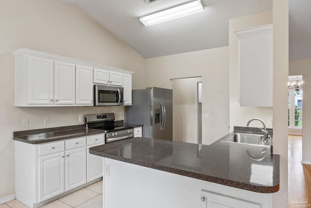kitchen featuring a peninsula, a sink, white cabinets, appliances with stainless steel finishes, and vaulted ceiling