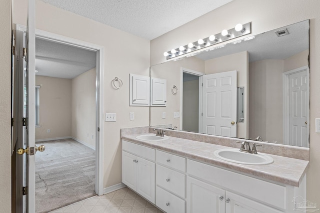 bathroom with a textured ceiling, visible vents, a sink, and double vanity