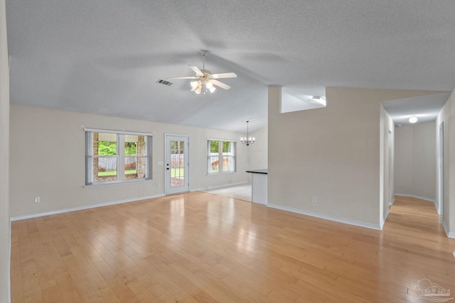 unfurnished living room with lofted ceiling, ceiling fan with notable chandelier, a textured ceiling, visible vents, and baseboards