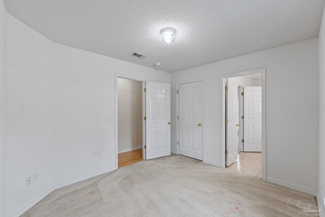 unfurnished bedroom with a textured ceiling, carpet flooring, baseboards, and visible vents