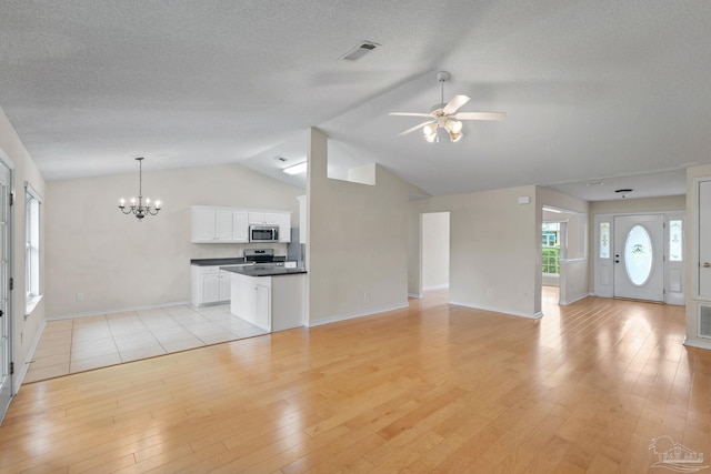 unfurnished living room with vaulted ceiling, ceiling fan with notable chandelier, light wood-type flooring, and baseboards