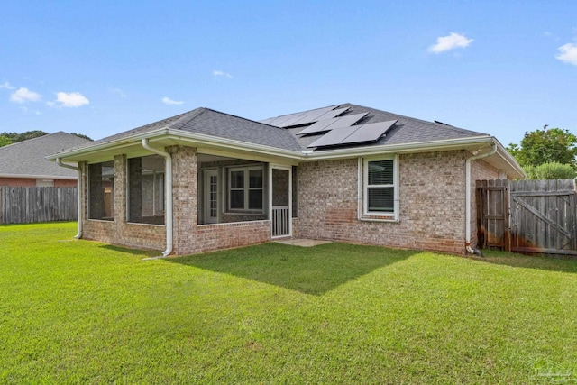 rear view of property with brick siding, a yard, a fenced backyard, solar panels, and a shingled roof