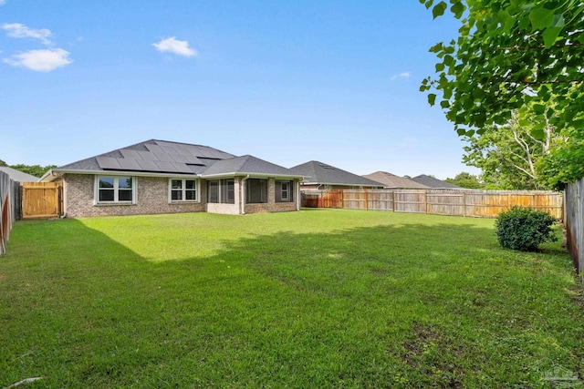 rear view of house with brick siding, solar panels, a lawn, and a fenced backyard