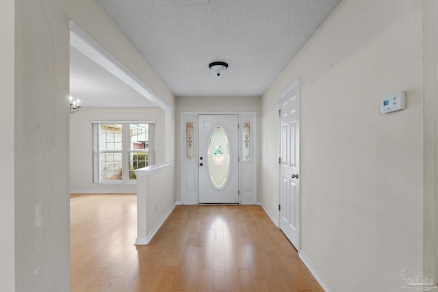 foyer entrance featuring a textured ceiling, baseboards, and light wood-style floors