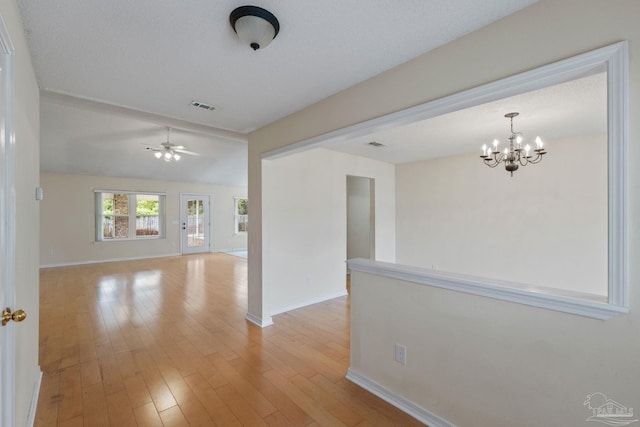 empty room featuring light wood-style floors, visible vents, baseboards, and ceiling fan with notable chandelier