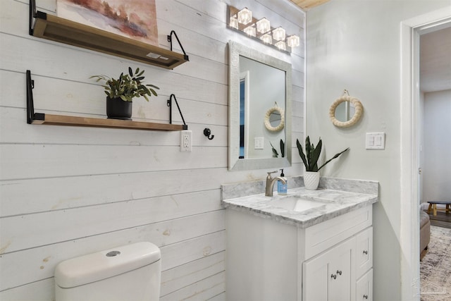 bathroom featuring vanity, wooden walls, and toilet