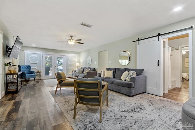 living room with french doors, ceiling fan, wood-type flooring, and a barn door