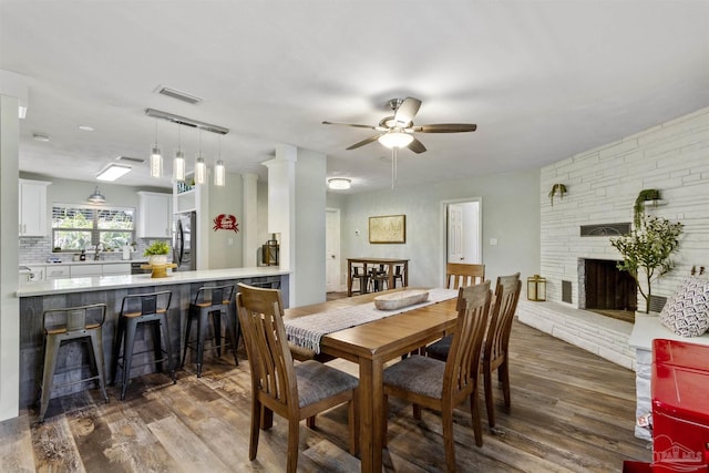 dining room with a fireplace, dark wood-type flooring, sink, and ceiling fan