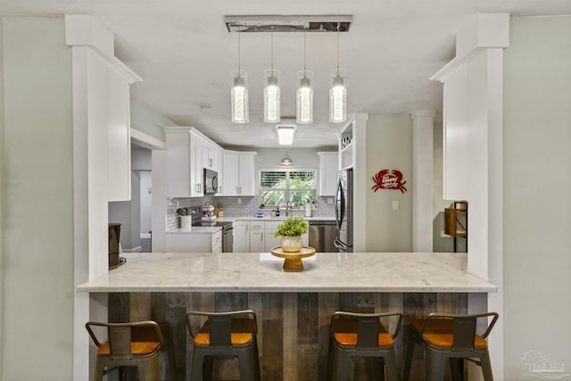 kitchen featuring a breakfast bar, white cabinetry, appliances with stainless steel finishes, kitchen peninsula, and backsplash