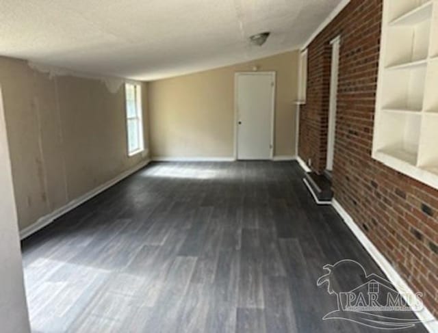 unfurnished room featuring a textured ceiling, brick wall, lofted ceiling, and dark hardwood / wood-style flooring