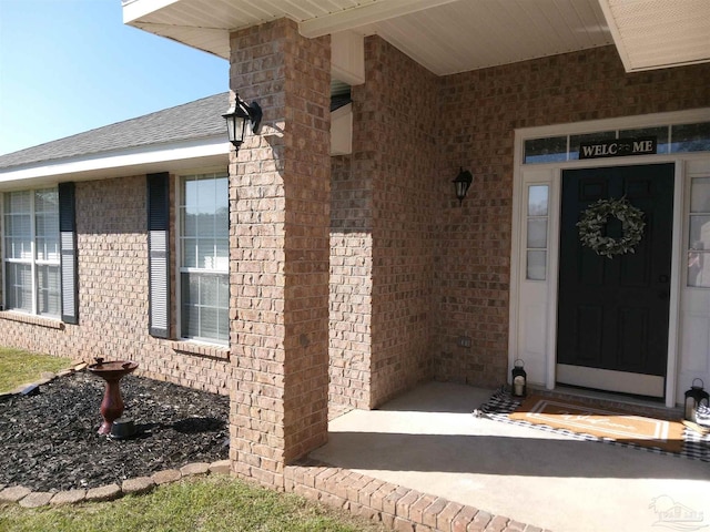 doorway to property featuring brick siding and roof with shingles