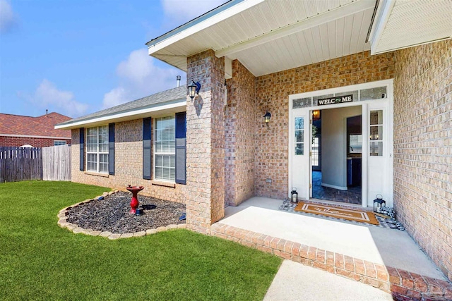 view of exterior entry featuring brick siding, a lawn, and fence