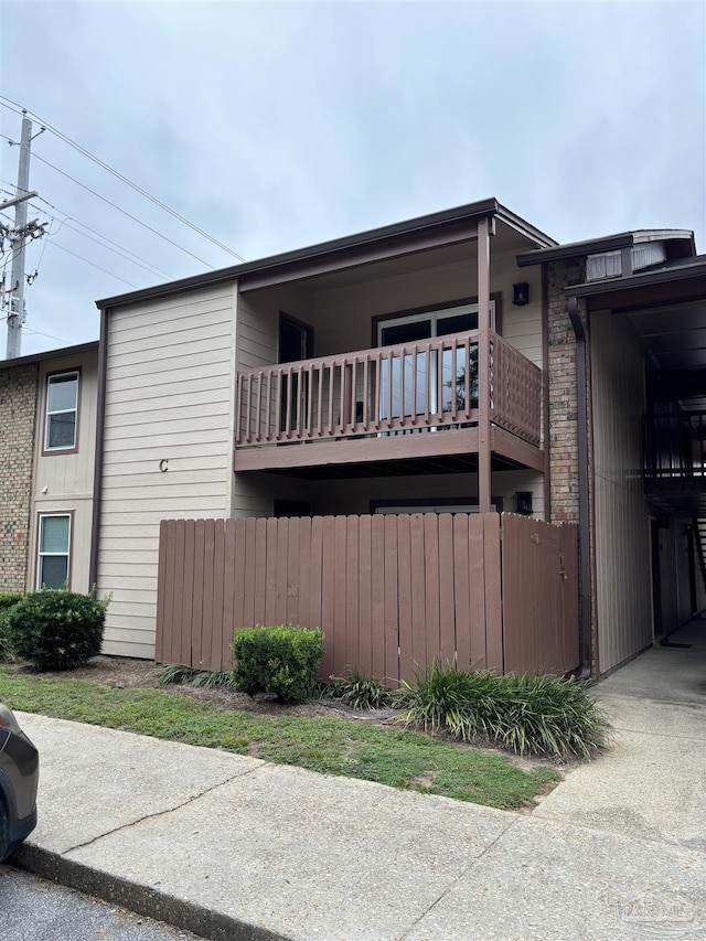 view of side of home featuring brick siding, fence, and a balcony