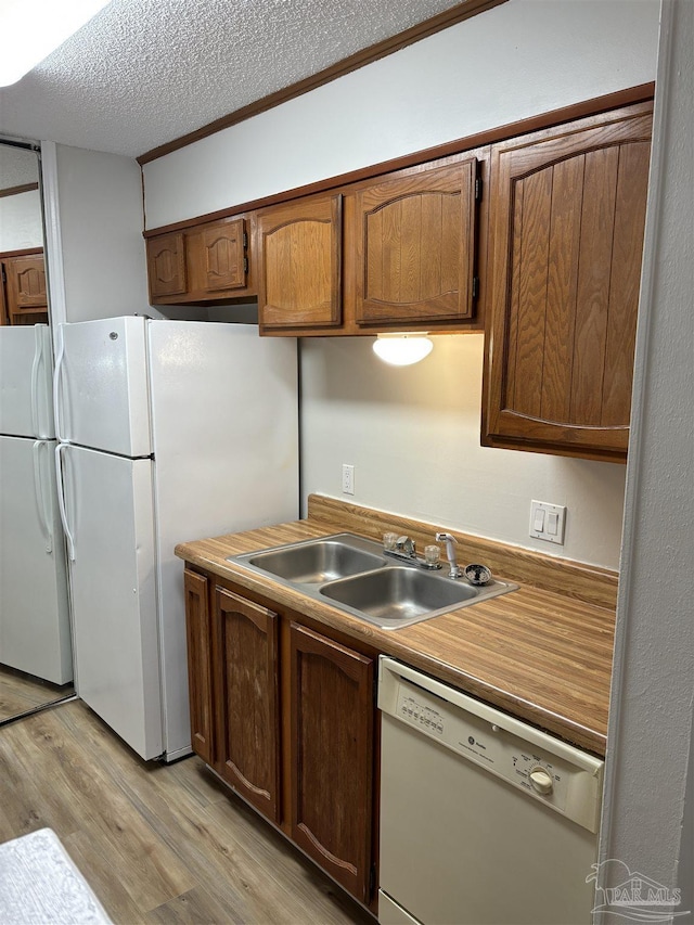 kitchen featuring brown cabinets, a sink, light wood-style floors, white appliances, and a textured ceiling