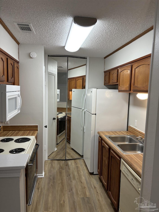 kitchen featuring visible vents, white appliances, a textured ceiling, a sink, and light wood finished floors