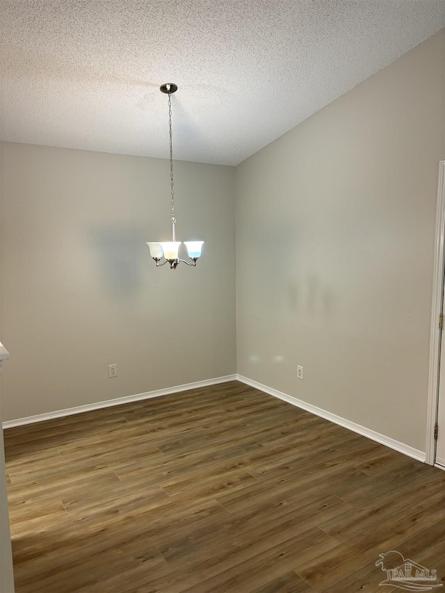unfurnished dining area with a textured ceiling, baseboards, a chandelier, and dark wood-style floors