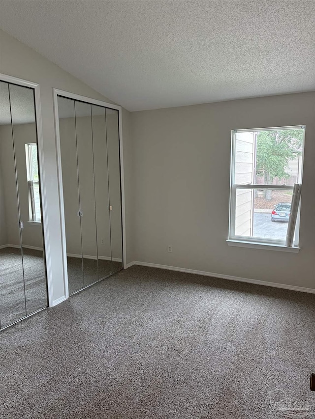 unfurnished bedroom featuring carpet floors, baseboards, a textured ceiling, and two closets