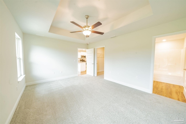 carpeted spare room featuring plenty of natural light, ceiling fan, and a raised ceiling