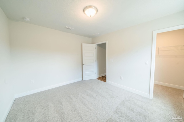 unfurnished bedroom featuring a walk in closet, a closet, and light colored carpet