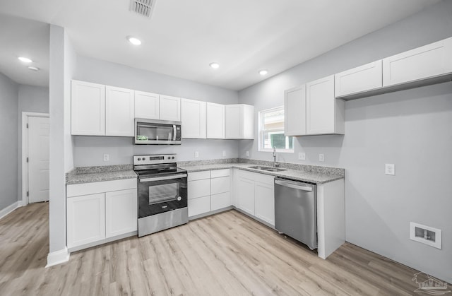 kitchen with appliances with stainless steel finishes, sink, white cabinets, and light hardwood / wood-style flooring