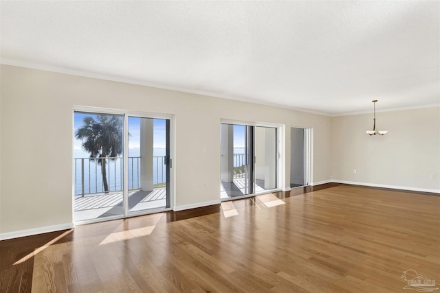 empty room with an inviting chandelier, hardwood / wood-style floors, ornamental molding, and a textured ceiling