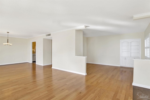 empty room with ornamental molding, a notable chandelier, light hardwood / wood-style floors, and built in shelves