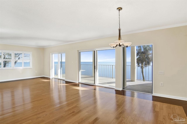 unfurnished room featuring an inviting chandelier, dark wood-type flooring, ornamental molding, and a water view