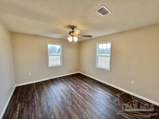 unfurnished room with dark wood-type flooring, visible vents, plenty of natural light, and baseboards