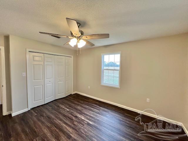 unfurnished bedroom featuring dark wood-type flooring, a closet, a textured ceiling, and baseboards