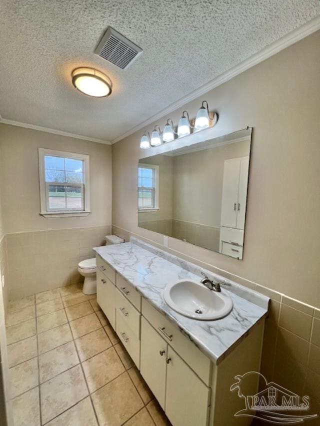 half bathroom with visible vents, ornamental molding, a textured ceiling, vanity, and tile walls