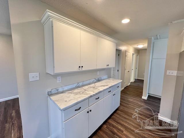 kitchen with dark wood-style floors, white cabinets, light stone counters, and baseboards