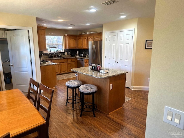 kitchen featuring a center island, dark hardwood / wood-style floors, dark stone countertops, decorative backsplash, and appliances with stainless steel finishes